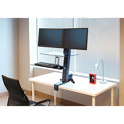 Office desk with two monitors, keyboard, and mouse. A lamp and a picture frame by the window.