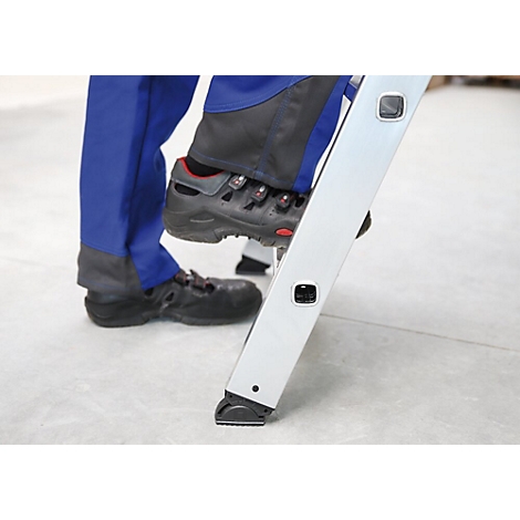 Personne montant sur une échelle. Chaussures de sécurité noires, vêtements de travail bleus. L'échelle est en métal.