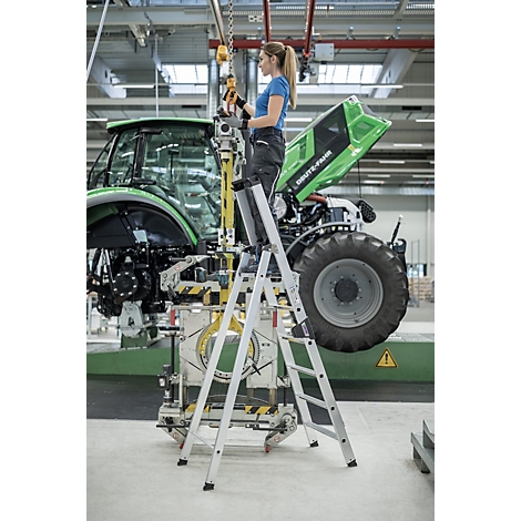 Une femme en tenue de travail est debout sur un escabeau, en train de travailler sur un tracteur. Le tracteur a des éléments verts et le logo "DEUTZ-FAHR".