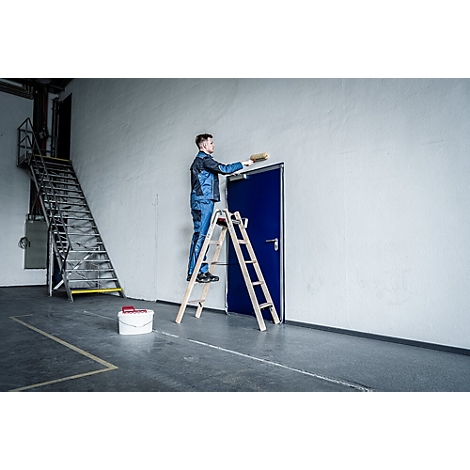 Un homme peint un mur. Il se tient sur une échelle, devant une porte bleue. Un seau clair à droite.