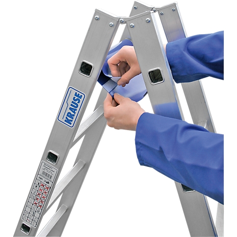 Persona plegando una escalera plateada. Lleva una camisa azul. El producto es de la marca Krause.