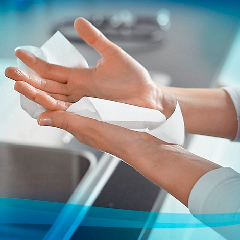 Les mains s'essuient avec une lingette blanche. Environnement lumineux avec un évier en arrière-plan.