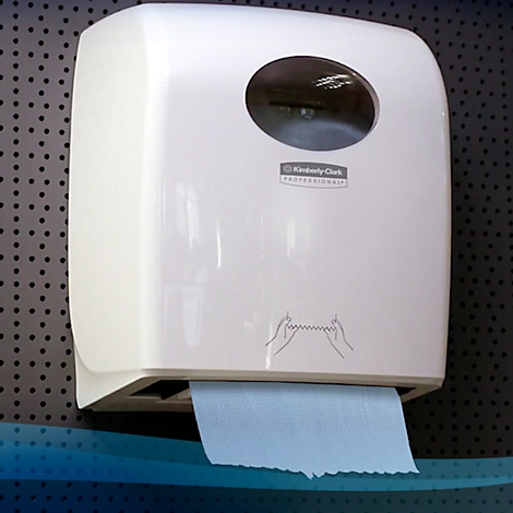 Distributeur d'essuie-mains en papier blanc avec essuie-mains en papier bleu, à côté d'une planche à trous noire.