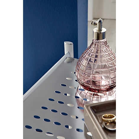 Flacon de parfum en verre rose sur une étagère perforée, à côté d'un plateau avec des bijoux.