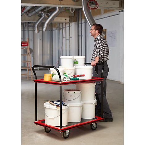 Een man duwt een rode gereedschapskar met verfemmers en gereedschap in een onafgewerkte ruimte.