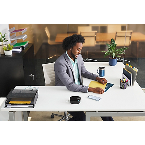 Un homme souriant en costume assis à un bureau, regardant des documents. Un téléphone, une tasse à café et des fournitures de bureau sont sur le bureau.