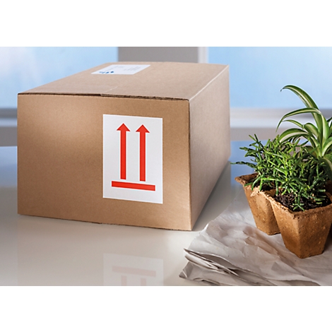 Une boîte en carton marron avec des autocollants. Des plantes et des couverts sont sur la table.