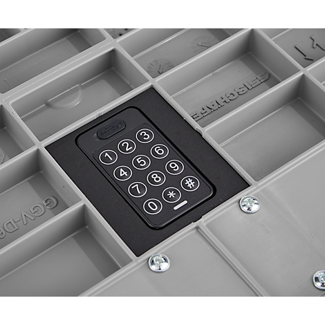 Detailaufnahme einer grauen Kunststoffbox mit einem schwarzen Tastenfeld mit Ziffern und Symbolen. Die Box hat mehrere Fächer.