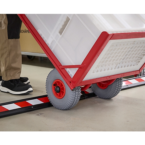 Nahaufnahme eines roten, rollbaren Transporters. Graue Reifen fahren über eine rot-weiß gestreifte Schiene.