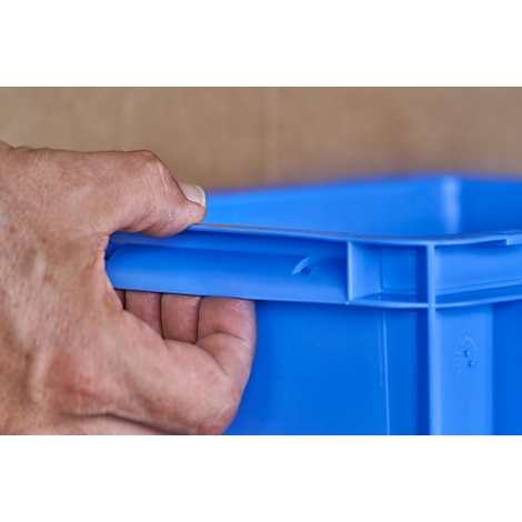 Close-up of a hand holding a blue plastic box by the handle.
