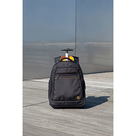 Schwarzer Trolley-Rucksack auf Holzuntergrund, vor einer grauen Wand.