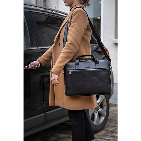 Femme avec une mallette noire debout près d'une voiture, ouvrant la portière. Elle porte un manteau marron et a le sac sur l'épaule.