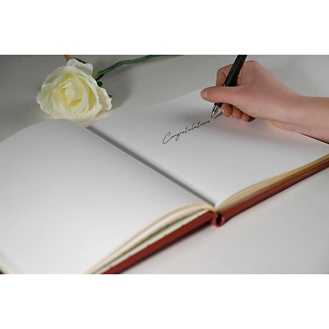 Een hand schrijft met een pen het woord "Congratulations" in een open rood notitieboekje. Daarnaast ligt een witte roos.