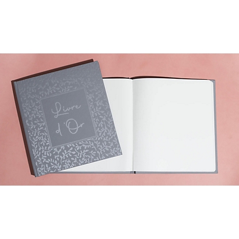 Livre gris intitulé 'Livre d'Or' posé ouvert sur fond rose.