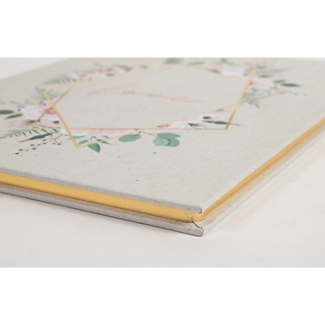 Un livre de couleur claire avec un motif floral et des accents dorés, photographié légèrement d'en haut.