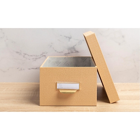 Boîte beige avec couvercle légèrement ouvert sur une surface en bois. Porte-étiquette sur le devant.