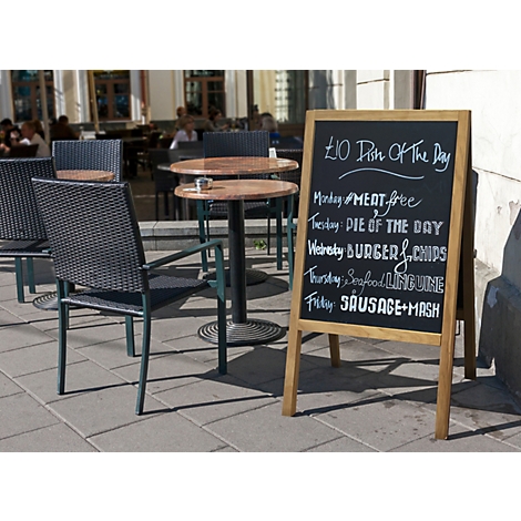 Un tableau de menu devant un café, indiquant les plats du jour : Meat Free, Burger & Chips, etc. Dehors, il y a des tables et des chaises.