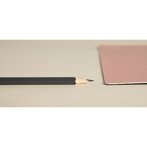 Ein Bleistift liegt neben einem rosafarbenen Papier auf einem beigen Untergrund. Die Bleistiftspitze ist scharf.