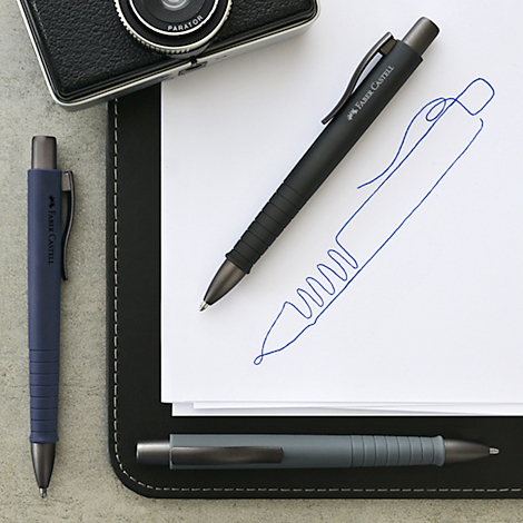 Drie balpennen op een tafel, waaronder een zwarte, een blauwe en een grijze pen.