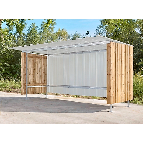 Bushaltestelle mit Holz- und Metallkonstruktion. Die Seiten sind mit Holz verkleidet, das Dach ist transparent. Im Hintergrund Bäume und blauer Himmel.