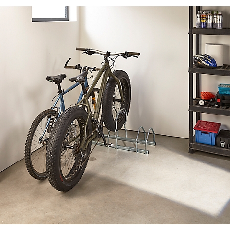 Zwei Fahrräder stehen in einer Garage in einem Fahrradständer. Eines ist ein Fatbike.