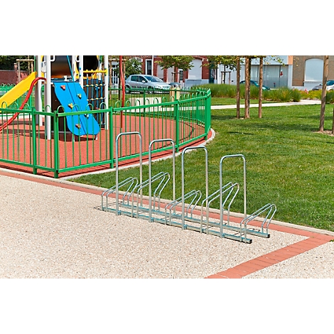 Fahrradständer auf einem Spielplatz; dahinter Spielgeräte und Rasen.