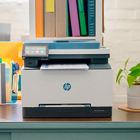 Weißer HP-Drucker mit Touchscreen. Auf dem Tisch liegen ein Blatt Papier und eine Topfpflanze.