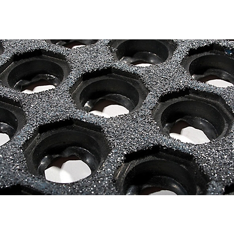 Close-up of a gray, hexagonal honeycomb structure. Black, circular recesses are in the honeycomb.