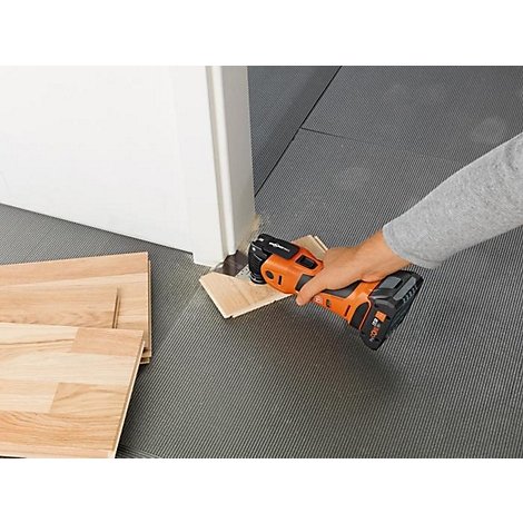 Une personne coupe un morceau de bois sous une porte avec un outil oscillant. D'autres morceaux de bois sont sur le sol.