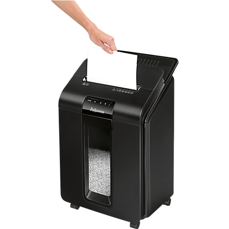 A hand inserts a white piece of paper into a black paper shredder. The shredder has a window showing shredded paper.