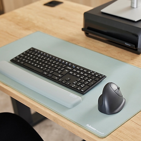 Een lachende vrouw zit aan een bureau met een computer, toetsenbord en plant.