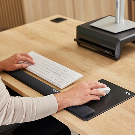 Man die werkt aan een in hoogte verstelbaar bureau. Hij zit in een bureaustoel en heeft een voetensteun.