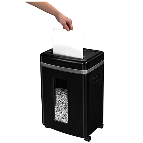 A hand inserting a white sheet of paper into a black paper shredder. Shredded paper is visible below.