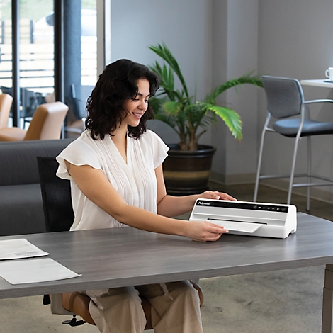 A woman inserts a sheet into a laminator, smiling.