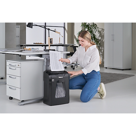 A young woman kneels, feeding paper into a shredder.