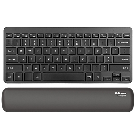 Femme assise à un bureau réglable en hauteur, tapant, souriant. Chaise de bureau grise, repose-pieds, moniteur. Configuration de bureau lumineuse.