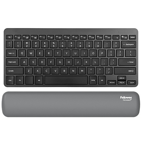 Un homme souriant est assis à un bureau. Il utilise une souris et un clavier, avec un écran devant lui. Il y a une plante sur la table.