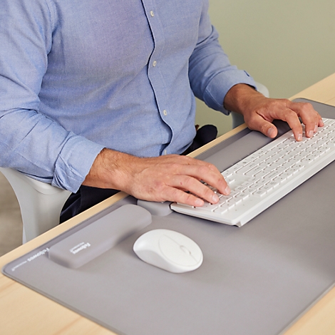 Mann am Schreibtisch mit weißer Tastatur und Maus, tippt. Graue Schreibtischunterlage mit Handgelenkstütze.