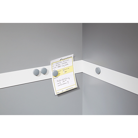 Gray magnets hold a note on a white strip on a gray wall. Text on the note is visible.
