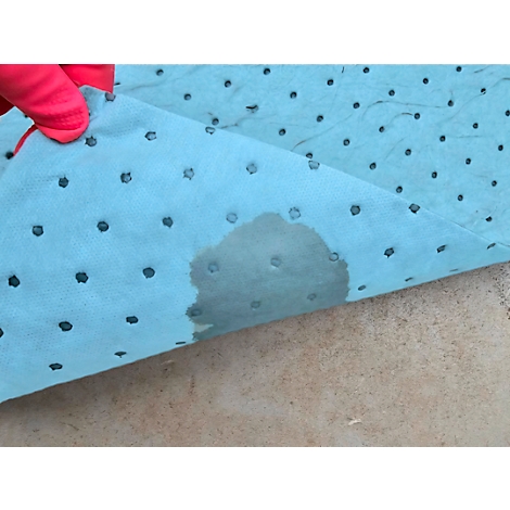 Un tapis absorbant l'huile bleu, dégoulinant, tenu par une main gantée de rouge, sur une surface claire.