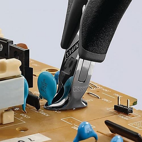 Une personne utilise une pince pour détacher un composant électronique d'une carte de circuit imprimé. L'outil est étiqueté 'NIPEX'.