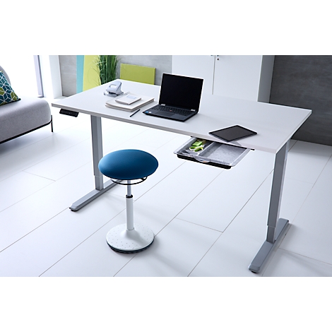 Ein höhenverstellbarer weißer Schreibtisch mit Laptop und ein blauer Hocker in einem modernen Büro.