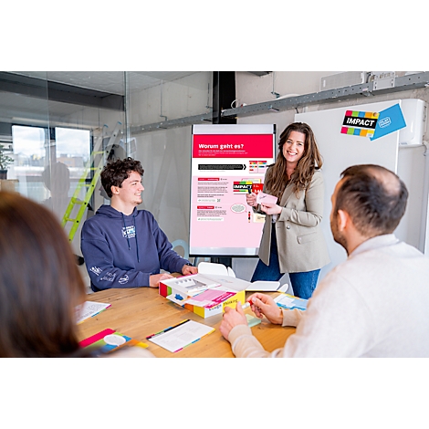 Eine lächelnde Frau präsentiert einem Team ein Produkt. Im Hintergrund eine Präsentation mit Text. Auf dem Tisch liegen weitere Produkte.