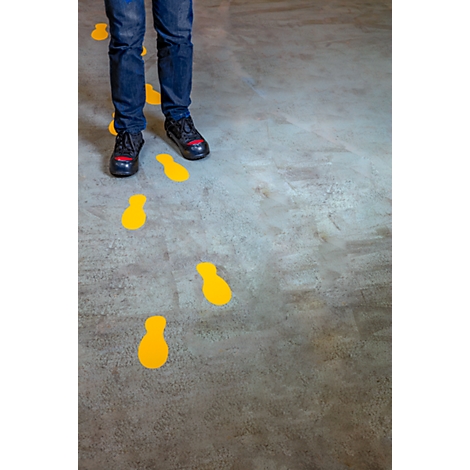 A child stands over yellow footprints on a gray floor. They are wearing jeans and black shoes with red accents.