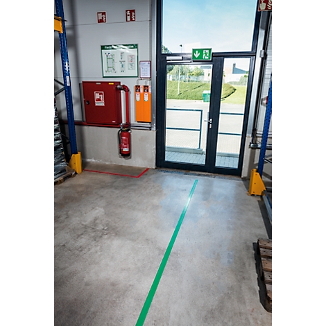 A green stripe leads to a door. On the wall are a fire extinguisher, signs, and an emergency exit marker.