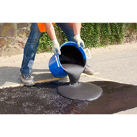 Person pours black asphalt from blue bucket onto street. Work clothes, gloves.