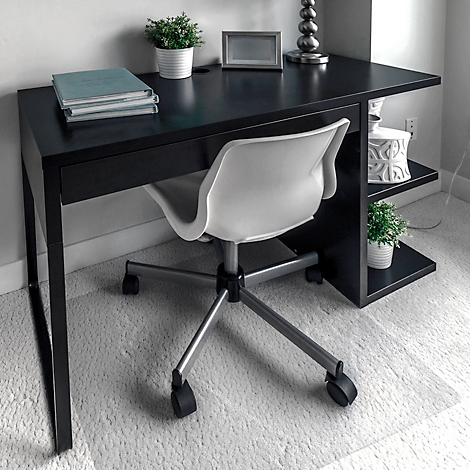 Bureau met bureaustoel. Op de tafel liggen boeken, een fotolijst en een lamp. Op een plank staan planten en een decoratie.