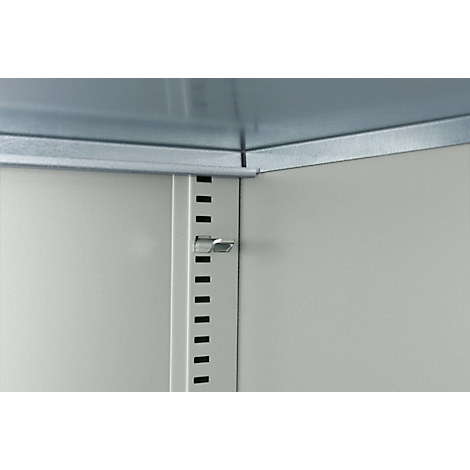 Innenansicht eines Metallschranks mit Beschlägen und Lochungen. Ein silberner Riegel hält die Schranktür geschlossen.