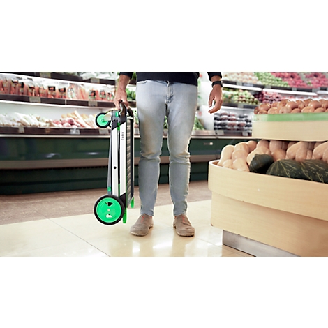 A person holding a folded shopping trolley in a grocery store. They are standing in front of vegetables and fruit.