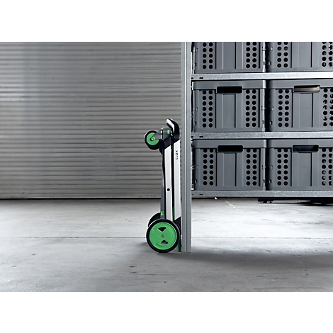 Foldable transport cart, green-black, standing next to a shelf with gray boxes.